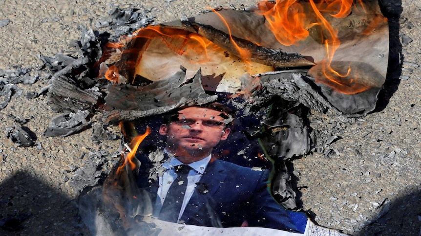 Protesters burn a photo of French President Emmanuel Macron.
