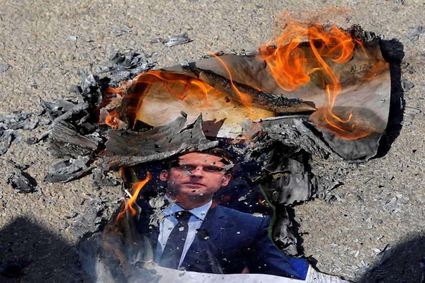 Protesters burn a photo of French President Emmanuel Macron.