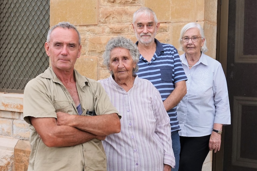 Four older people – two men and two women – stand outside a historic-looking building.