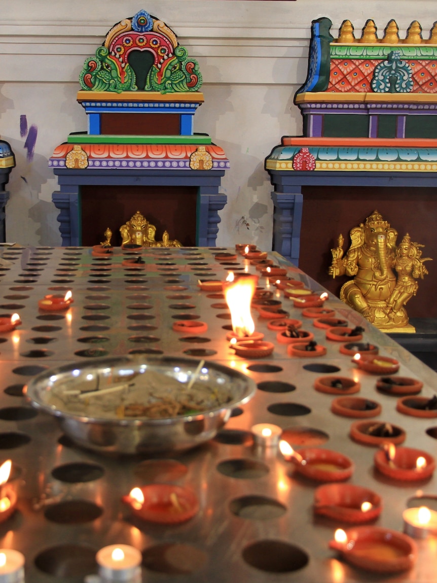Candles sit in front of a colourful Hindu shrine.