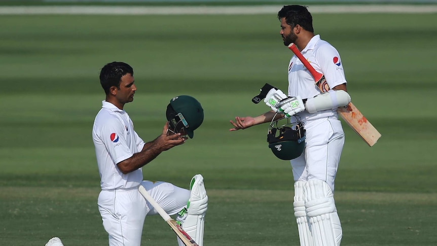 Fakhar Zaman kneeling looking at his helmet as he talks to Azhar Ali during the second Test in Abu Dhabi.
