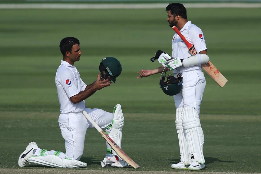 Fakhar Zaman kneeling looking at his helmet as he talks to Azhar Ali during the second Test in Abu Dhabi.