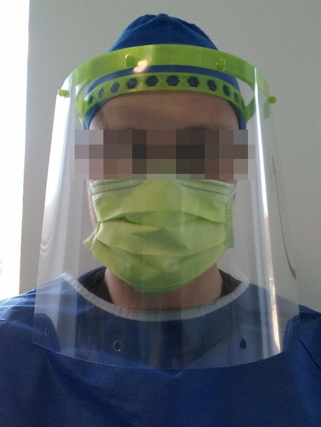 A man with eyes blurred wearing a perspex face shield.