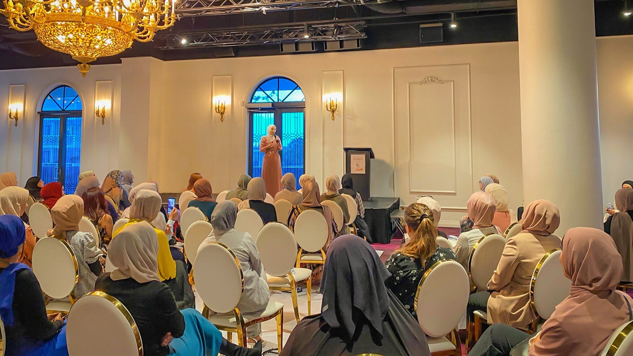 A woman standing on a stage in front of couple of women.