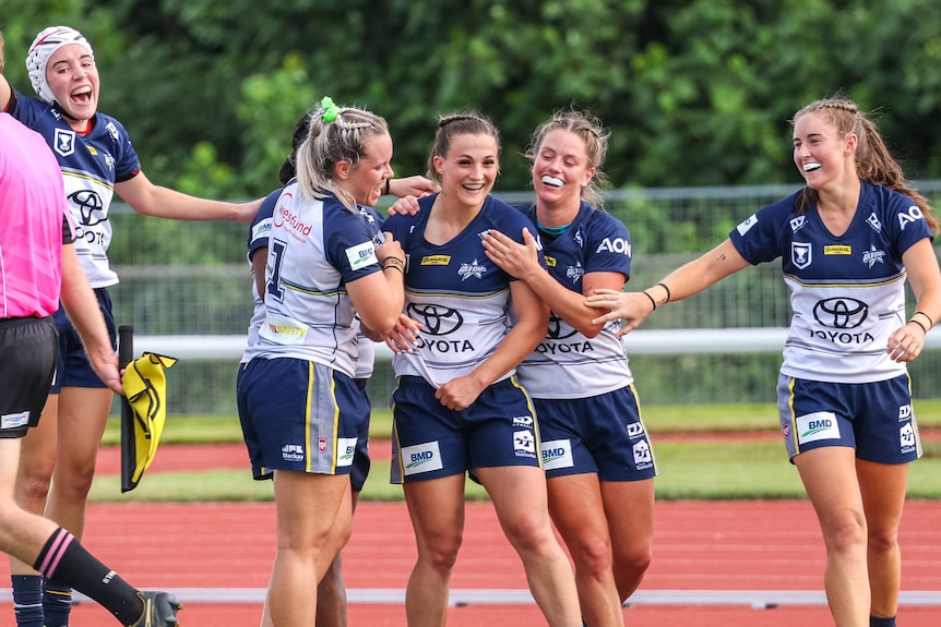 Women in rugby jerseys smile and congratulate a player on field