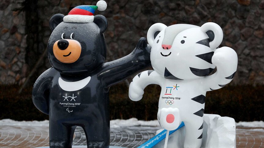 A statue of a cartoon black bear wearing a beanie next to a statue of a cartoon white tiger on a snow-covered footpath.