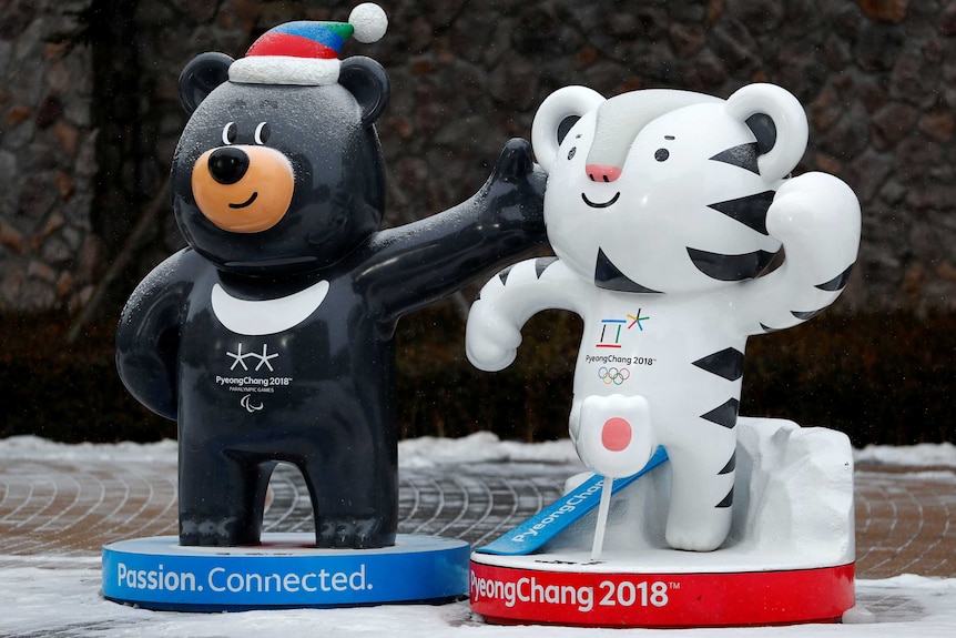 A statue of a cartoon black bear wearing a beanie next to a statue of a cartoon white tiger on a snow-covered footpath.