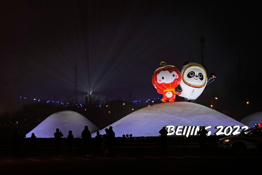 A lantern mascot and a panda bear mascot stand above a Beijing 2022 sign
