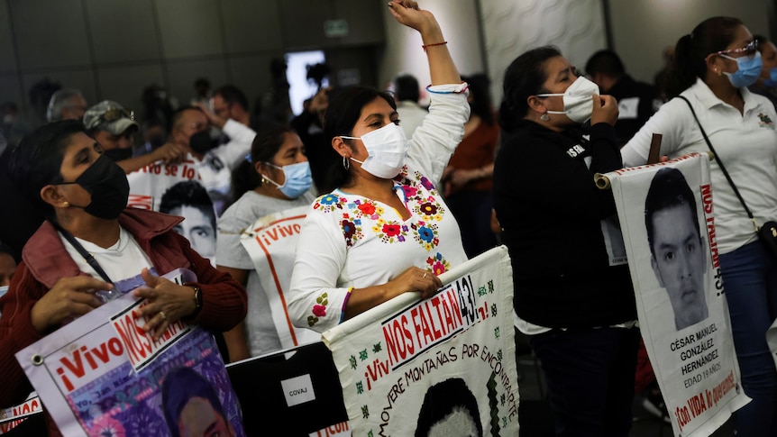 People wearing face masks and carrying signs with the faces of young men protest in a group 