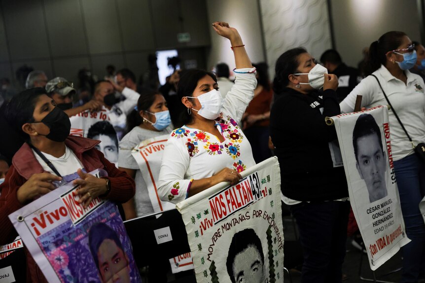People wearing face masks and carrying signs with the faces of young men protest in a group 