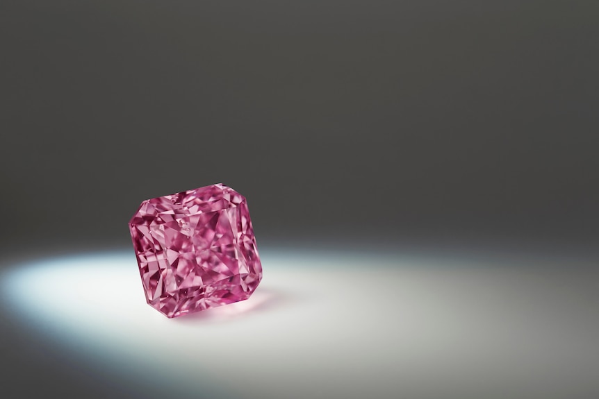 This glistening, square, radiant-cut diamond is also spotlit from the left in a dark space.