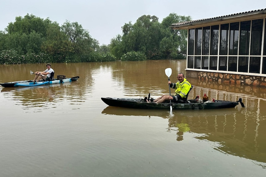 Two men in canoes in flood waters in the outback.  