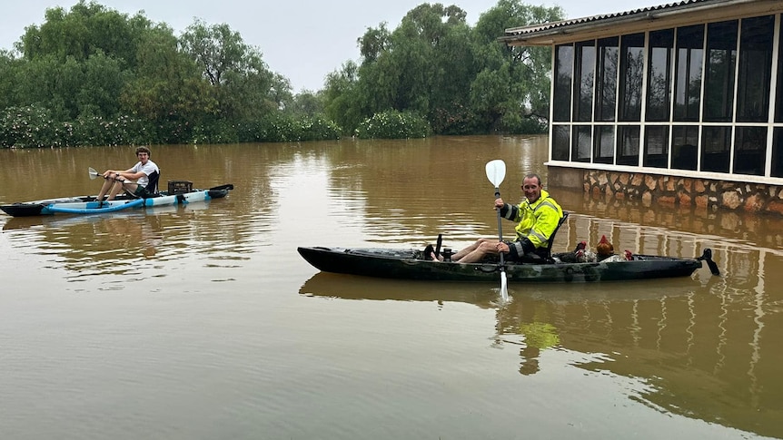 Two men in canoes in flood waters in the outback.  