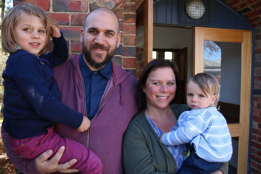 Two parents hold their two young child outside St Andrews Uniting Church in Fairfield, in Melbourne.