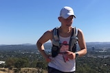 A woman runs on a dirt path with a blue sky in the background.