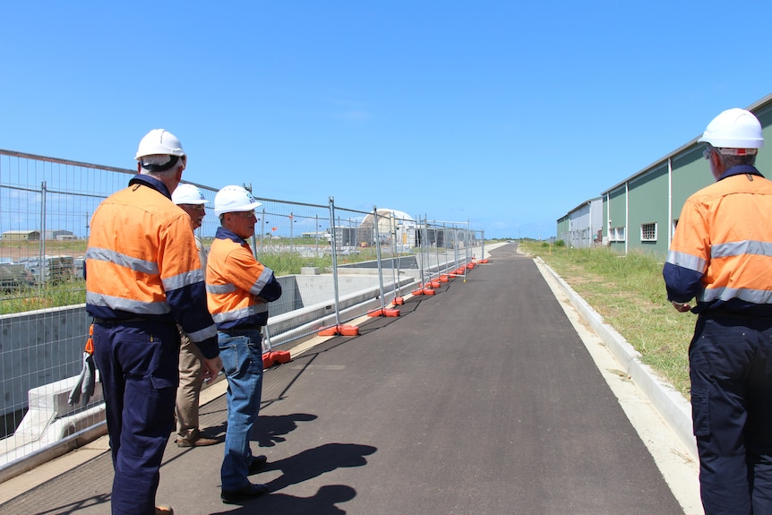 The backs of men looking down a tarmac runway, scaffolding on the left, blue sky
