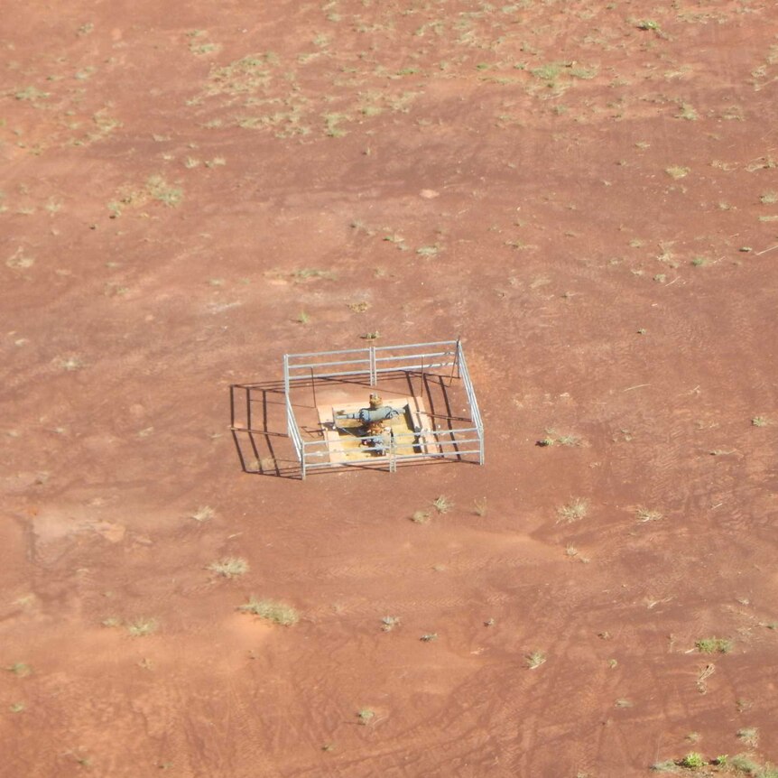 A capped well, which appears as a square opening on the ground with a fence around it, in the middle of empty, arid land.