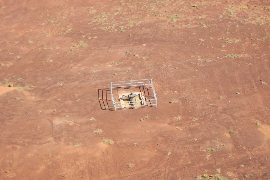 A capped well, which appears as a square opening on the ground with a fence around it, in the middle of empty, arid land.