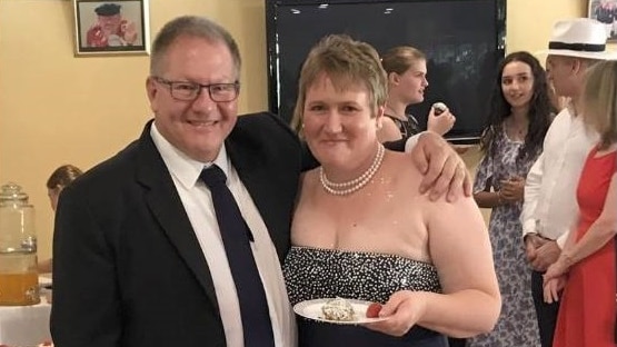 A man in a suit and a woman in a dress holding a plate with cake on it