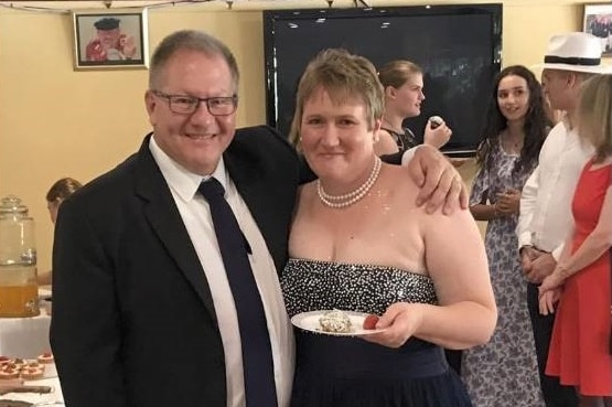 A man in a suit and a woman in a dress holding a plate with cake on it