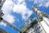 An external shot of a zinc factory looking up towards a blue sky and white clouds.