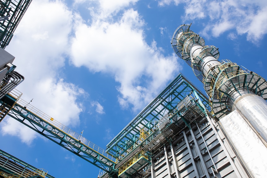 An external shot of a zinc factory looking up towards a blue sky and white clouds.