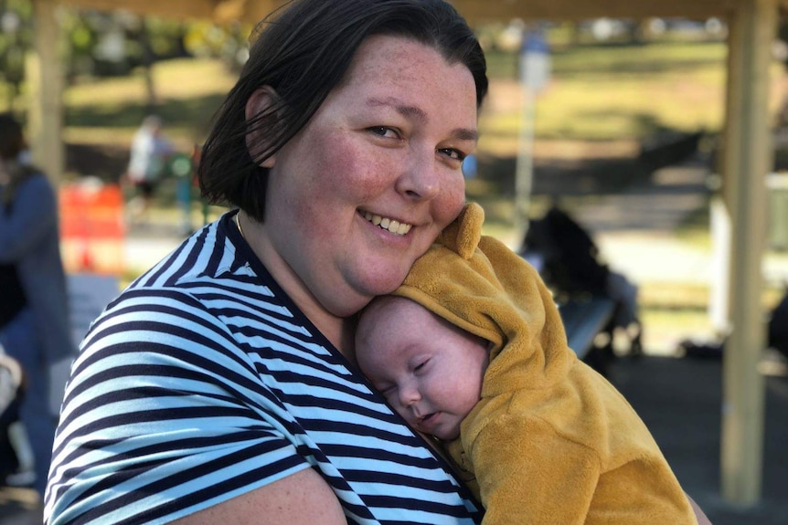 A woman cuddling a little baby to her chest in a park