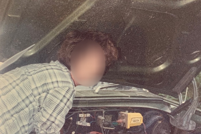 A man working on a car. His face is blurred out.