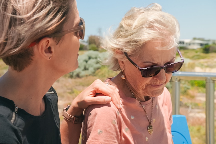 A younger woman has her hand on the shoulder of an older woman.