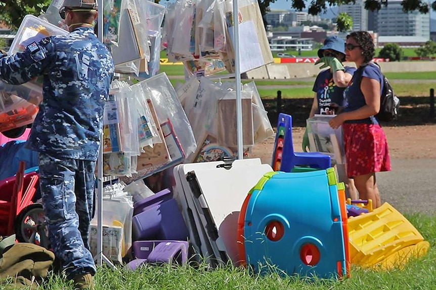 Two mums stand watching as RAAF personnel add damaged toys to a large pile