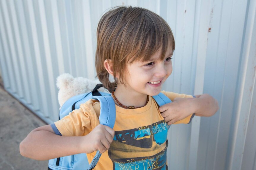 A young boy wearing a backpack smiles.