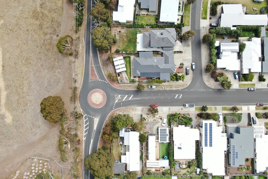 An aerialbirdseye view shot showing a road separating housing and a piece of undeveloped land.