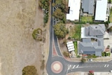 An aerialbirdseye view shot showing a road separating housing and a piece of undeveloped land.