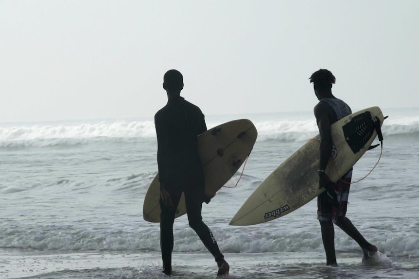 Two Ivorian surfers watch the waves with backs to camera