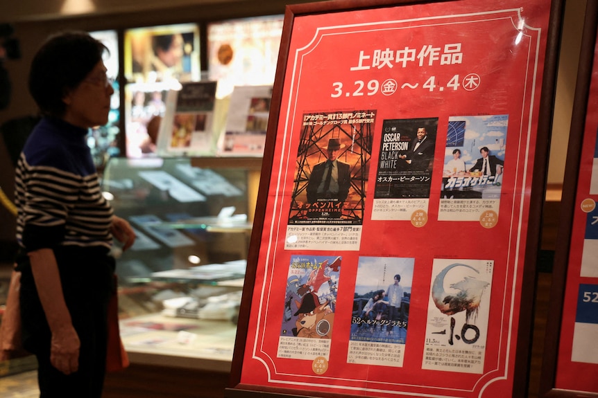 A woman looks at a list of movies on a poster.