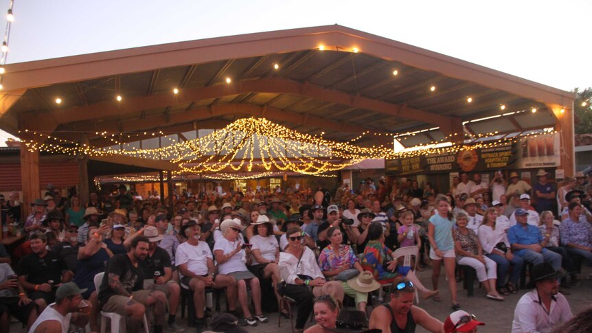 a crowd of people in a shed under fairy lights.