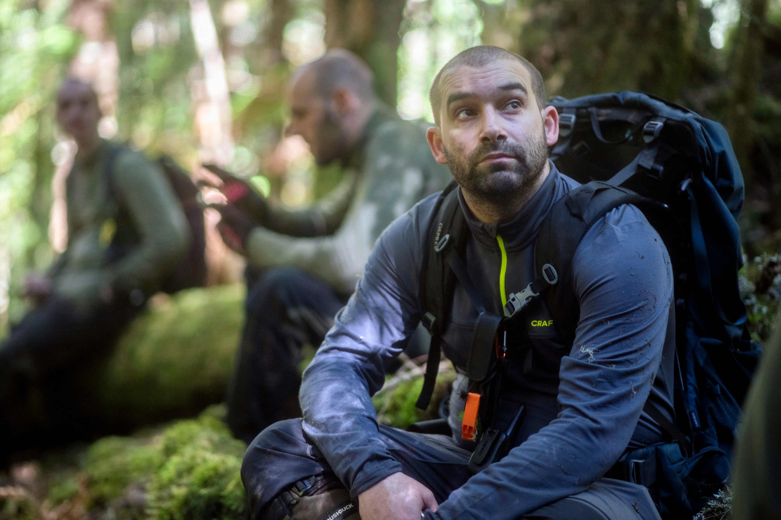 Gabriel Remy se agazapa en lo profundo del bosque con su equipo de senderismo y mira al cielo. Detrás de él hay dos visores.
