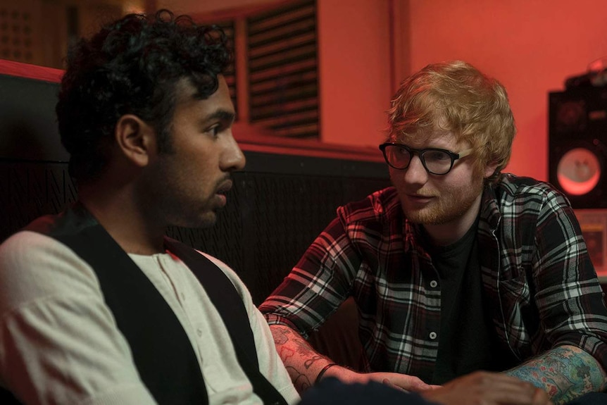 Patel, in a white shirt and waistcoat, listens intently as Sheeran explains something to him, studio gear in the background.