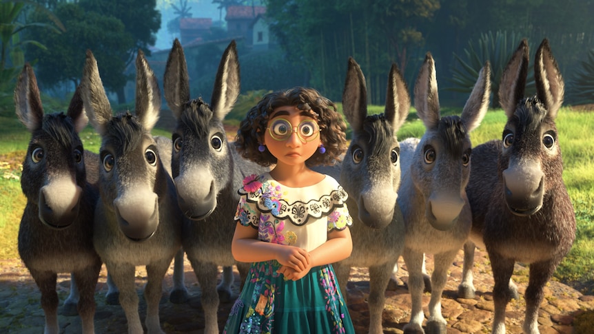 Animated brown girl with big glasses, curly dark hair, butterfly-patterned white blouse and teal skirt stands with six donkeys.
