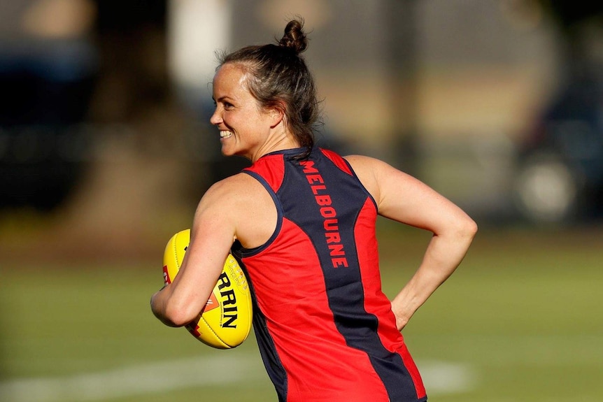 Daisy Pearce in a Melbourne club singlet, holding a ball and smiling at training.
