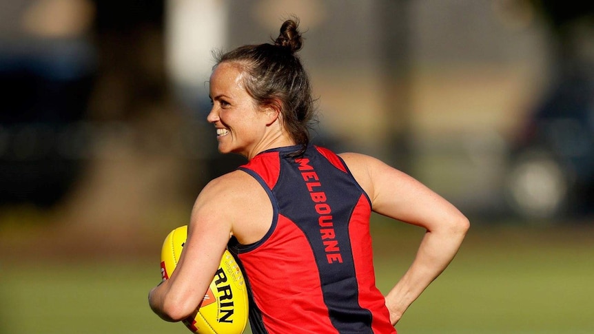 Daisy Pearce in a Melbourne club singlet, holding a ball and smiling at training.
