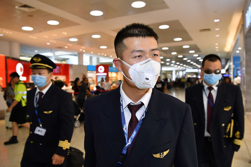 Three male flight crew wear masks as they walk through Sydney airport