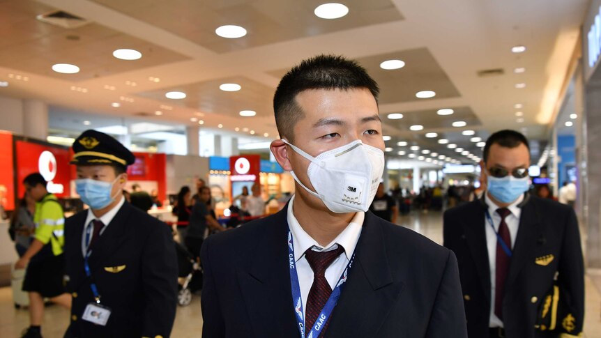 Three male flight crew wear masks as they walk through Sydney airport