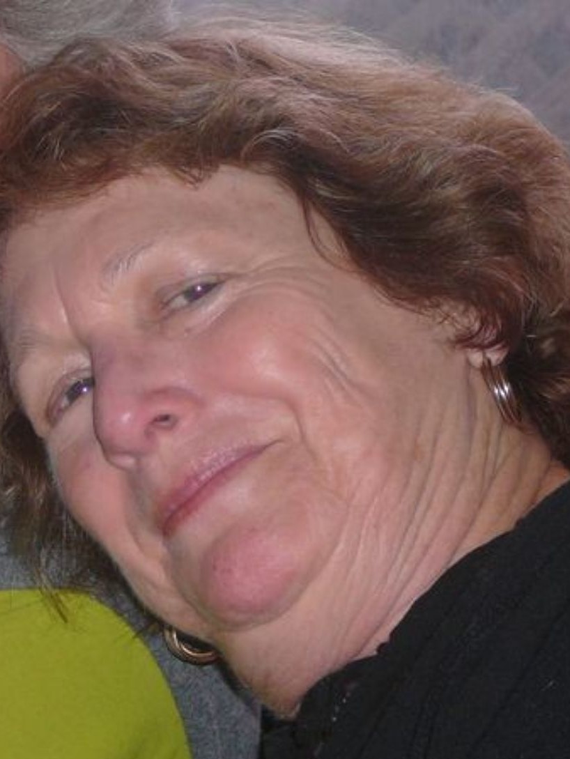 A closeup portrait of a woman with brown hair, head tilted and smiling at the camera.