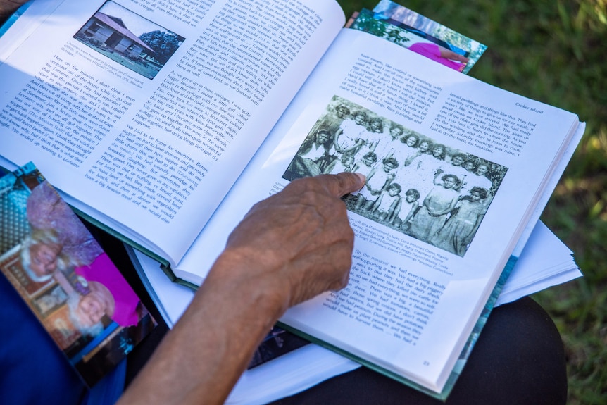 A woman pointing to a photo in a history book. 