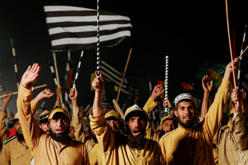 Una folla di uomini vestiti di giallo che camminano e tengono le loro bandiere bianche e nere durante una manifestazione