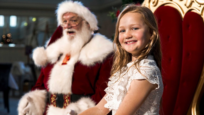 santa claus talking and smiling at a young girl in a white dress