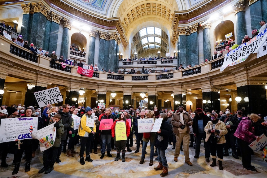 Protesters stand in an ornate circular hall holding pro choice signs. 