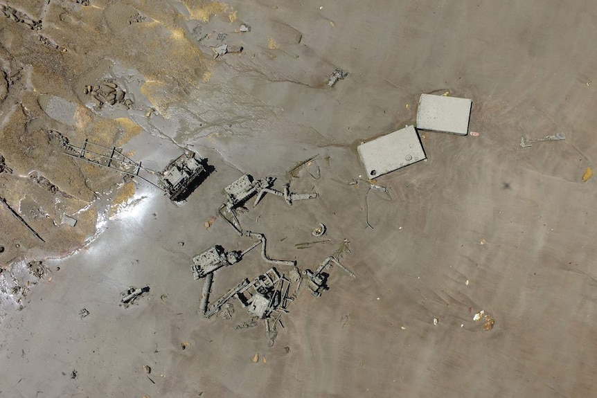 An aerial shot of some pieces of an old ship in low-tide mud.