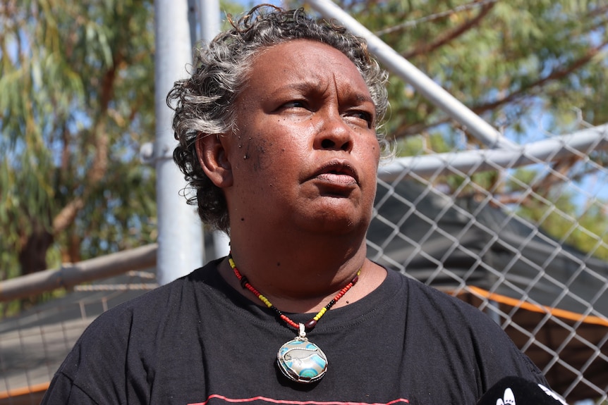 A woman looks beyond the camera as she stands in front of a wire fence.